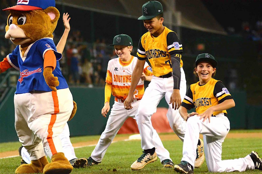 Peachtree City Little League’s Tai Peete and Charlie Clem dance along side Southwest’s Charlie Wylie and Little League Mascot Dugout before the two teams play in an elimination game. Photo/Brett Crossley.