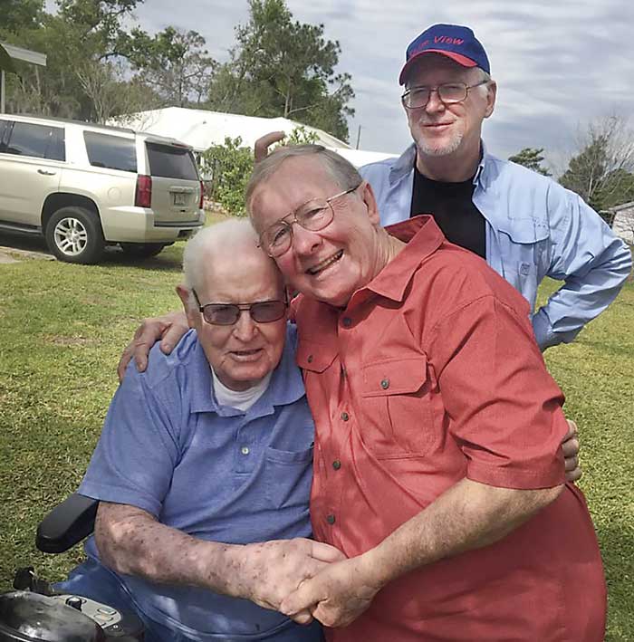 Senoia resident Bob Lisle (in red shirt) gives his biological father, 88-year-old Floyd Sheffield, a hug as the two meet for the first time in March in Winterhaven, Fla. Standing nearby is Bob’s brother, Jeff Sheffield. Photo/Submitted.
