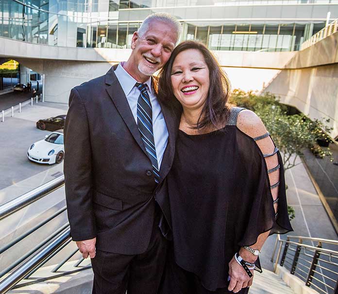 As guests depart for their thrill rides in the background, Doreen Ward and Glen Pinyann are pictured on the stairway to the Porsche Experience Center terrace level during the 2nd annual Drive & Dine event benefitting Christian City Children & Family Programs. Photo / Chris Rank Photography