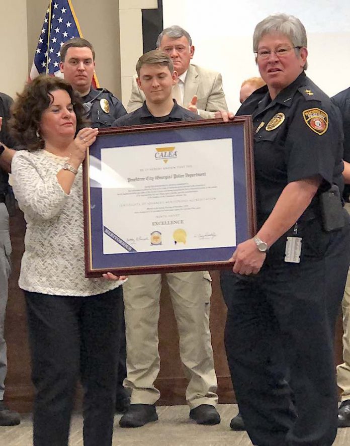 Backed by members of the Peachtree City Police Department, Mayor Vanessa Fleisch (L) and Chief Janet Moon display the award announcing the department's recent accreditation again by CALEA. Photo/Cal Beverly.