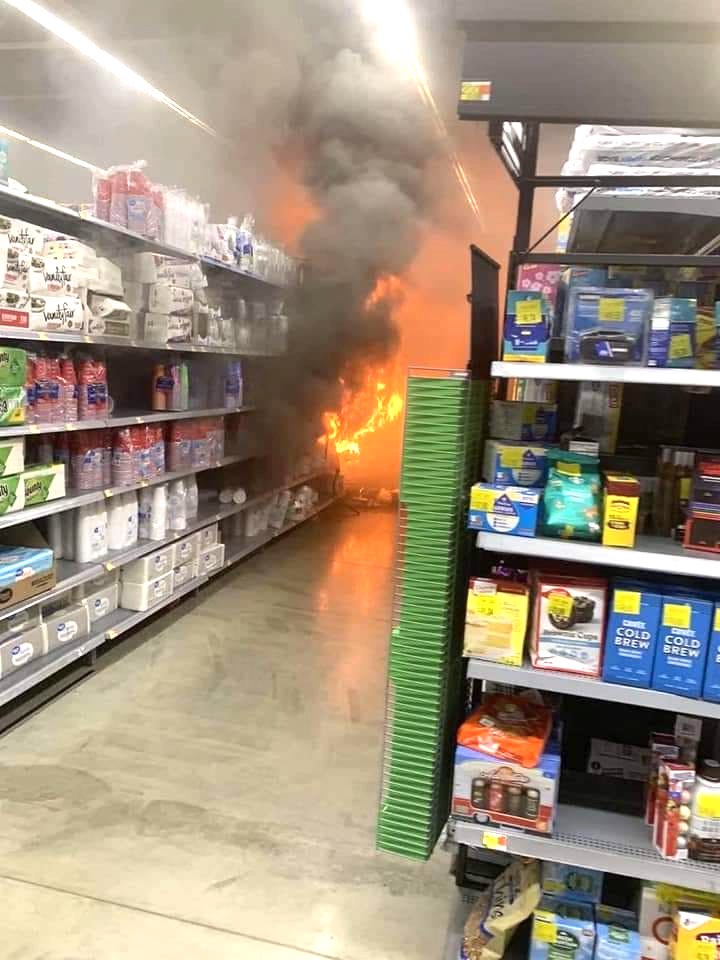 Vlammen schieten uit een rek in het gangpad met papieren producten zoals toiletpapier en papieren borden naar de achterkant van de Walmart Superstore in Peachtree City.  De foto werd genomen vlak nadat het vuur oplaaide en werd gedeeld op de Facebook-pagina van de Peachtree City Police Department.